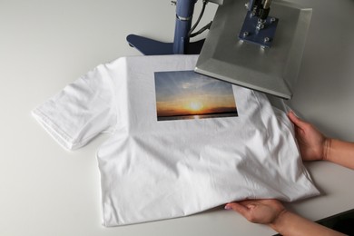 Custom t-shirt. Woman using heat press to print image of beautiful landscape
