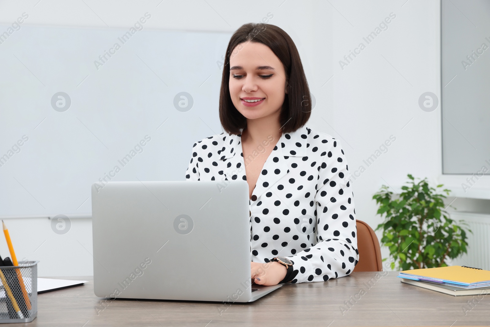 Photo of Happy young intern working with laptop at table in modern office