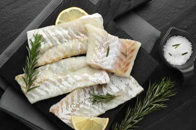 Photo of Fresh raw cod fillets, rosemary, lemon and salt on black table, flat lay