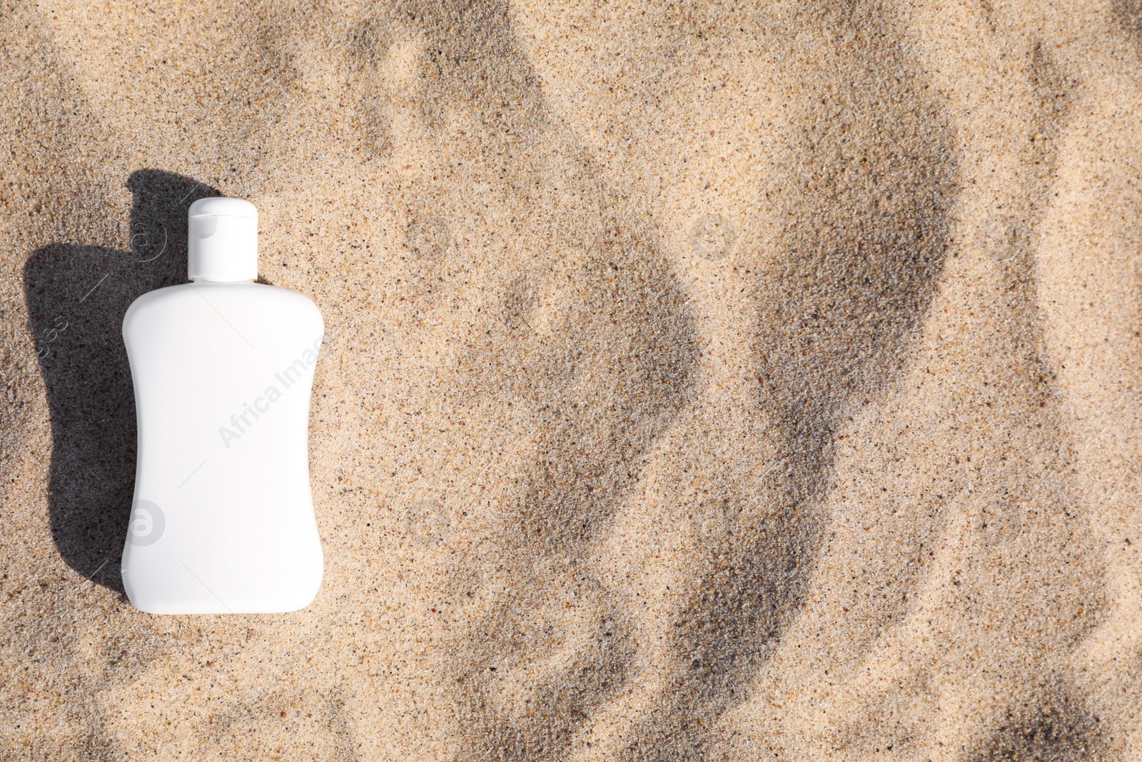Photo of Blank white bottle of sunscreen on sand, top view. Space for text