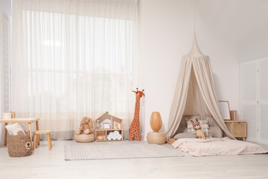 Photo of Cozy kids room with play tent, toys and comfortable floor bed. Montessori interior