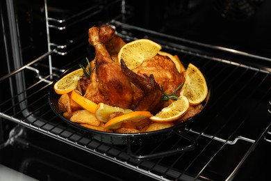Photo of Baked chicken with orange slices and rosemary in oven