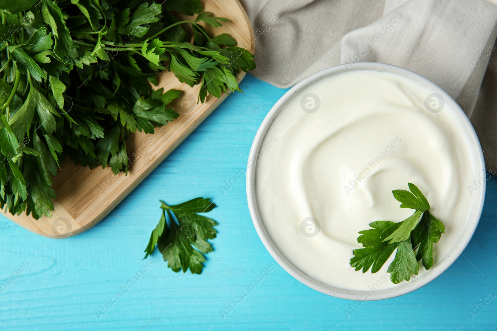 Photo of Flat lay composition with sour cream and parsley on light blue wooden table