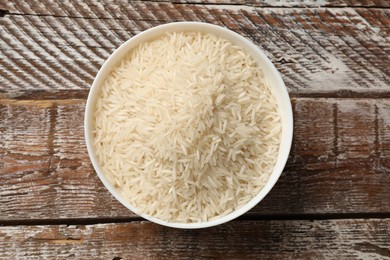 Photo of Raw basmati rice in bowl on wooden table, top view