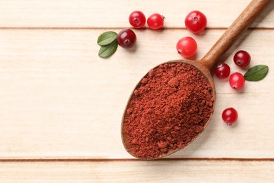 Dried cranberry powder in spoon, fresh berries and green leaves on light wooden table, top view. Space for text