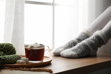 Photo of Woman and cup of hot winter drink near window indoors, closeup