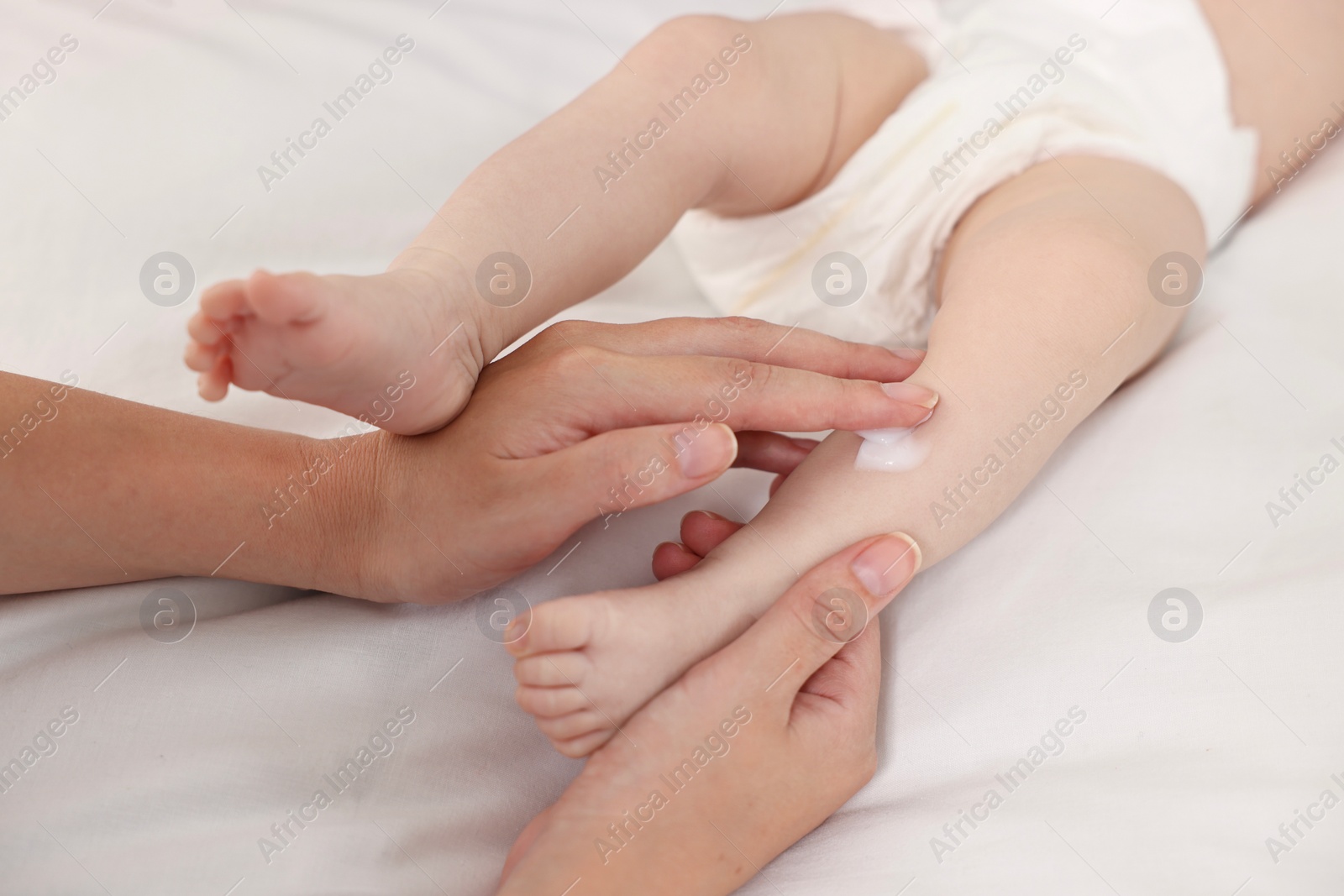 Photo of Woman applying body cream onto baby`s skin on bed, closeup