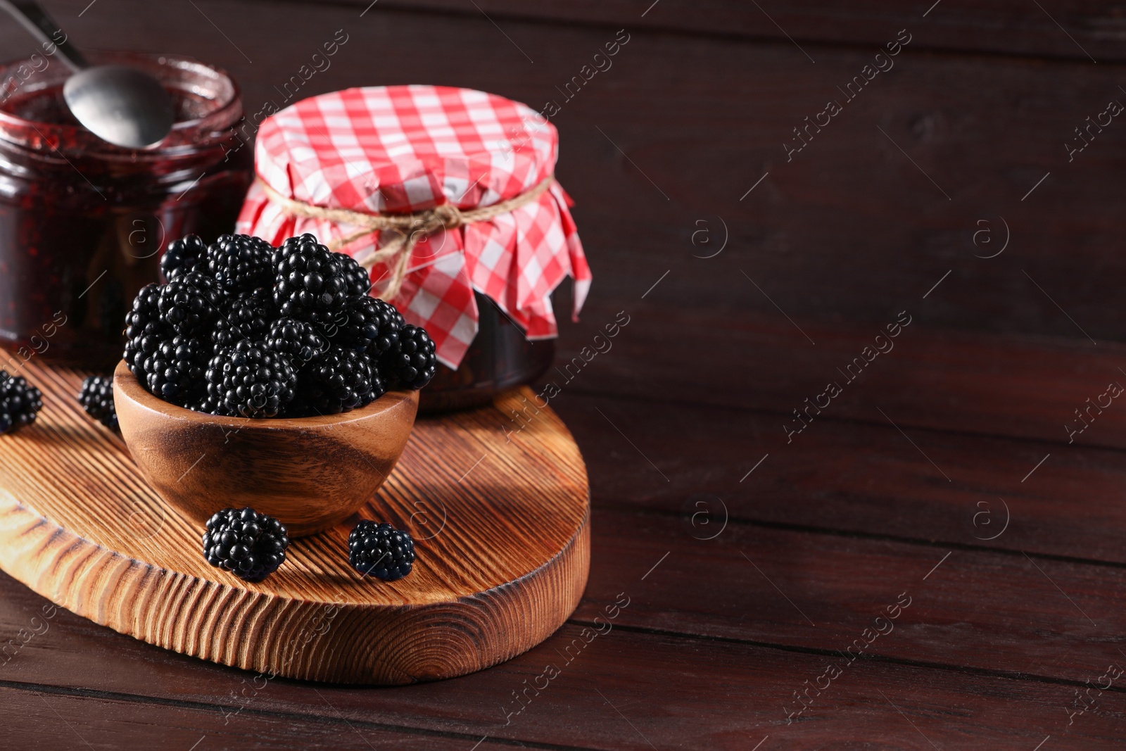 Photo of Fresh ripe blackberries and tasty jam on wooden table. Space for text