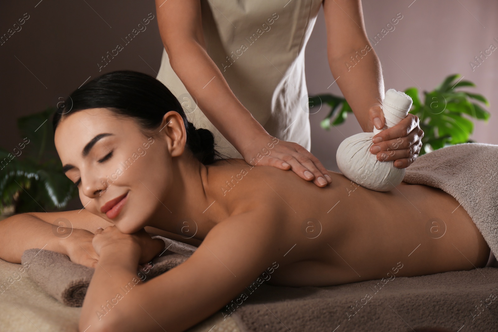 Photo of Young woman receiving herbal bag massage in spa salon