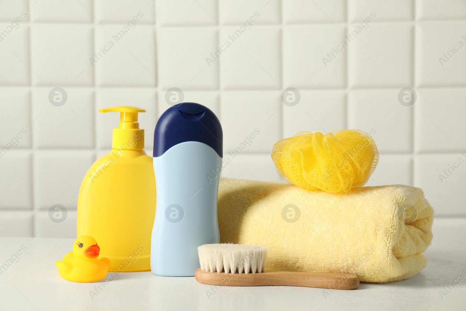 Photo of Baby cosmetic products, bath duck, brush and towel on white table against tiled wall