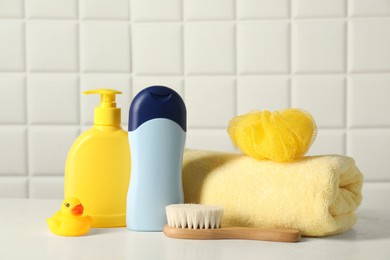 Baby cosmetic products, bath duck, brush and towel on white table against tiled wall