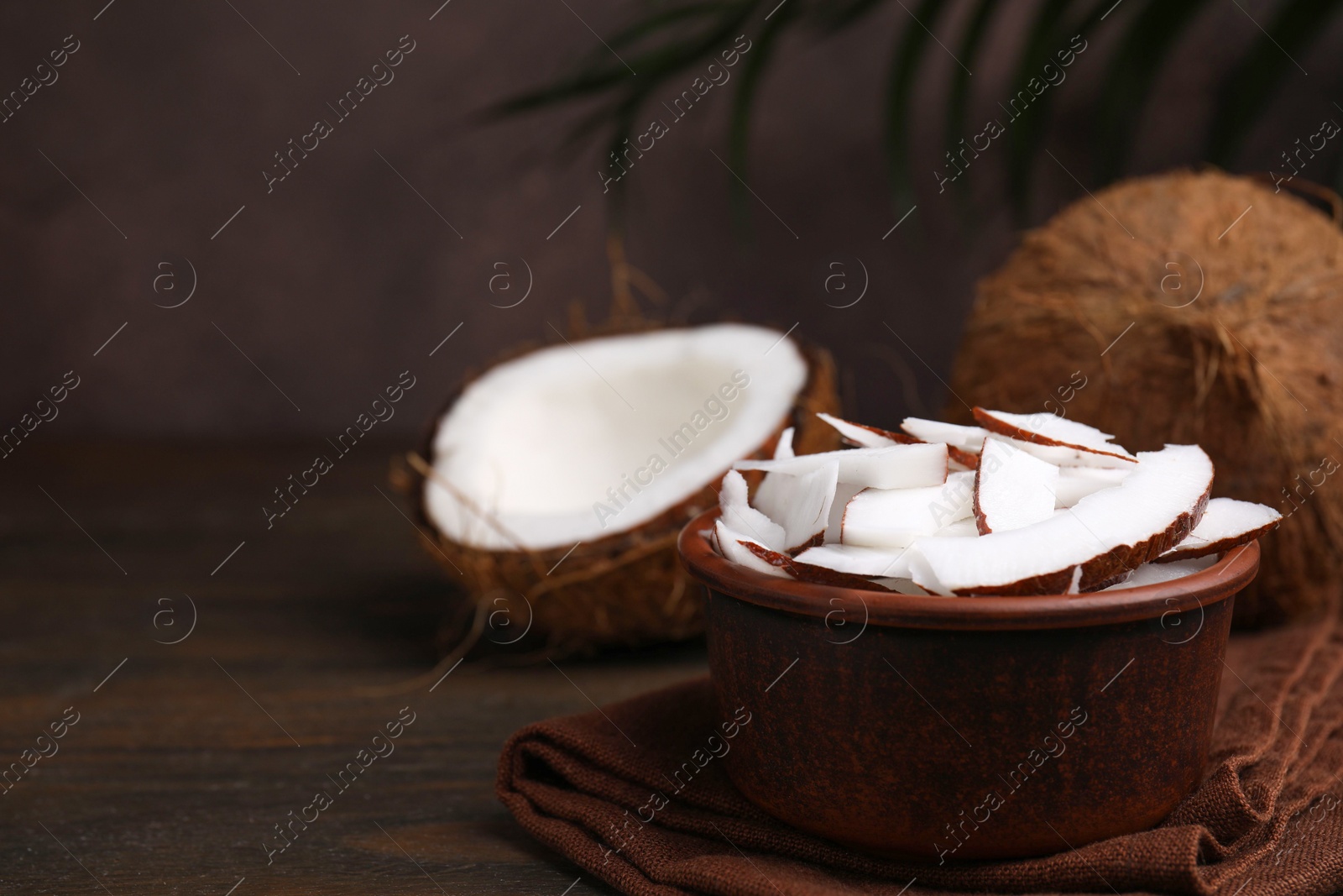 Photo of Coconut pieces in bowl and nuts on wooden table, space for text