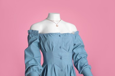 Female mannequin dressed in stylish light blue dress with necklace on pink background