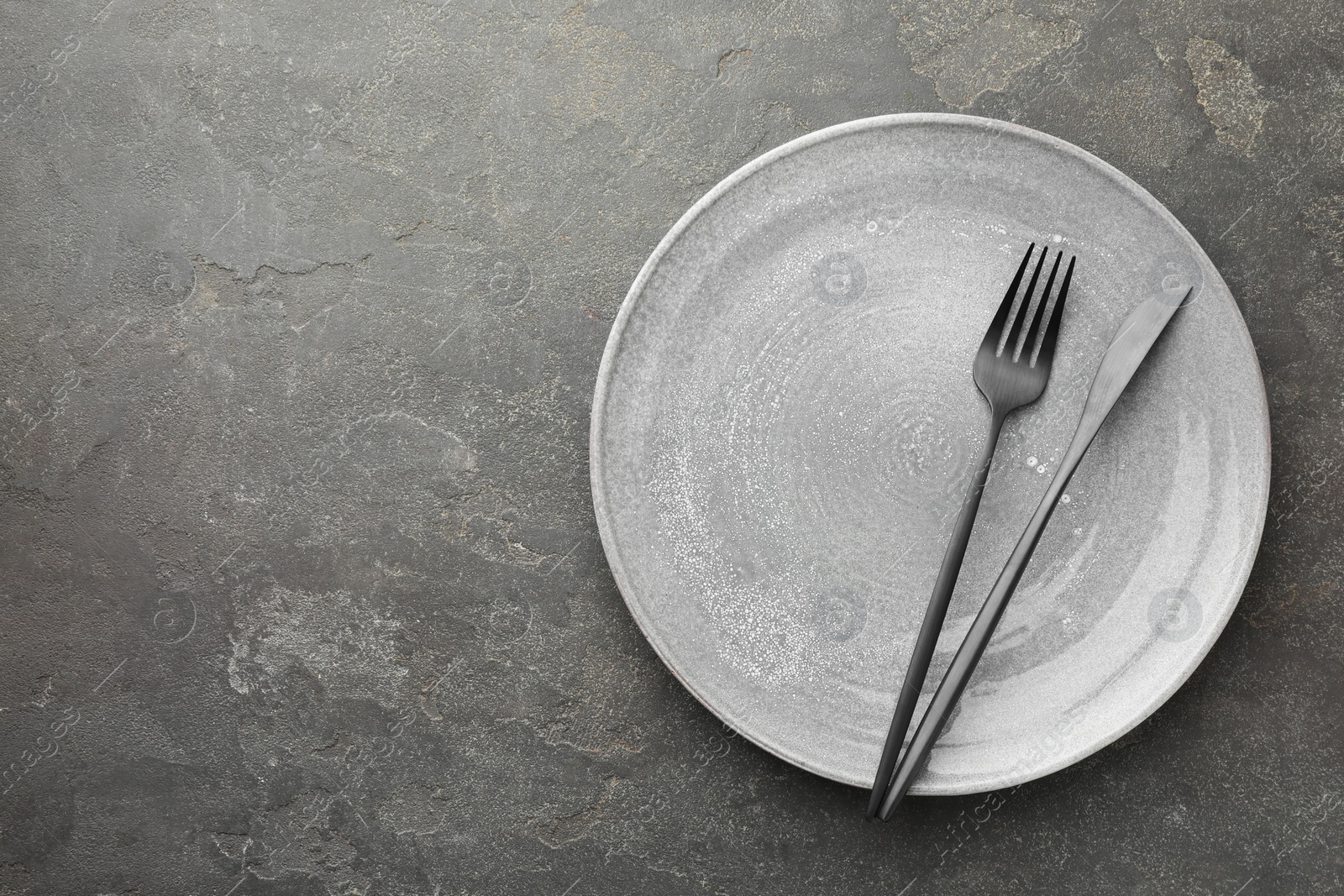 Photo of Clean plate and cutlery on grey textured table, top view. Space for text