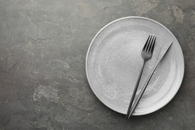 Clean plate and cutlery on grey textured table, top view. Space for text