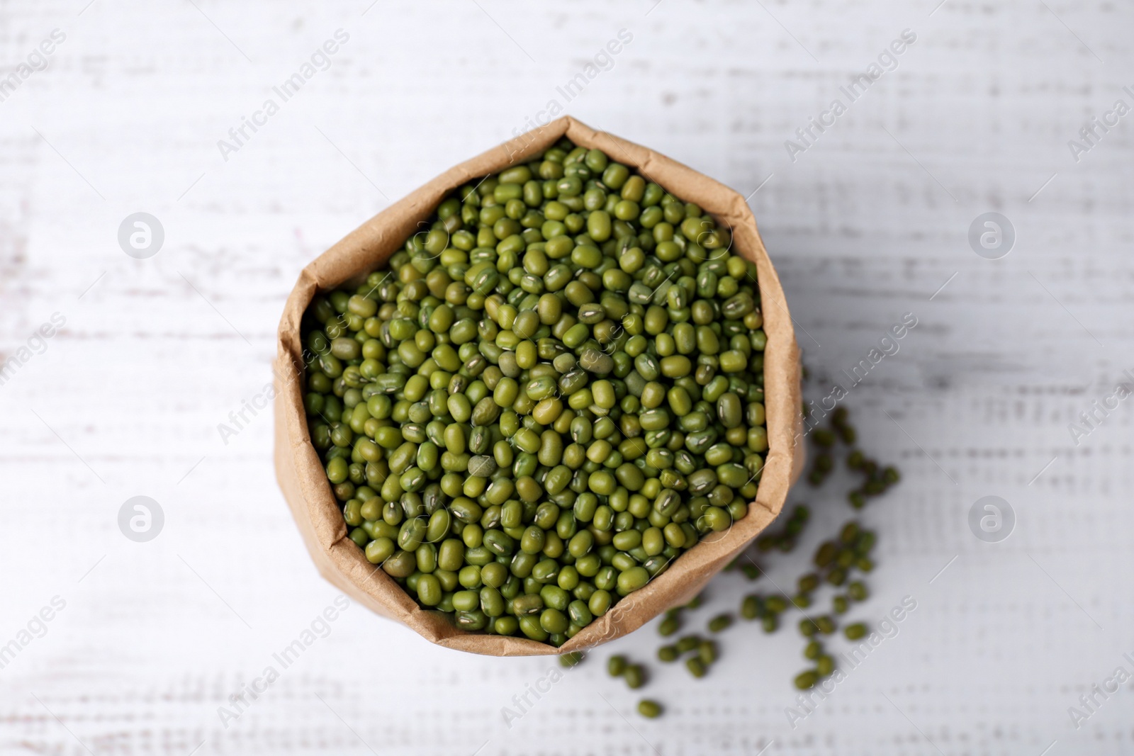 Photo of Paper bag with green mung beans on white wooden table, top view