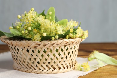 Photo of Fresh linden leaves and flowers in wicker basket on wooden table,