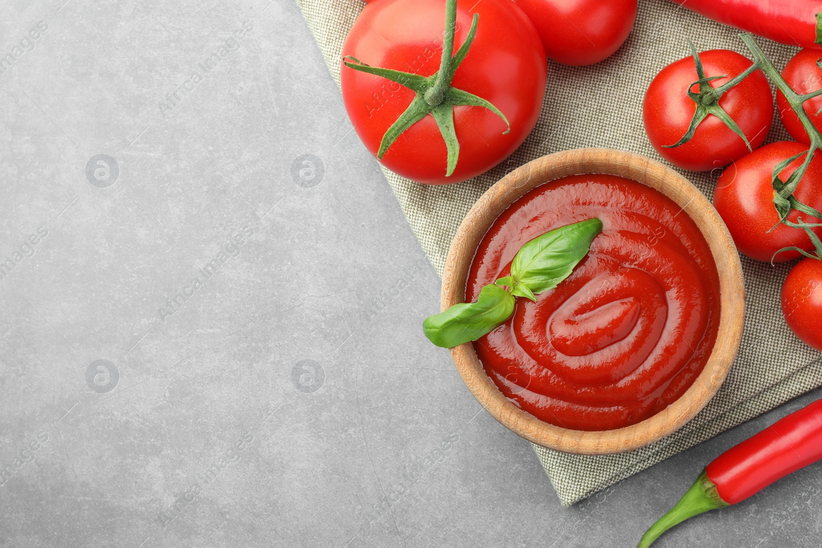 Photo of Bowl of tasty ketchup and ingredients on light grey table, flat lay. Space for text