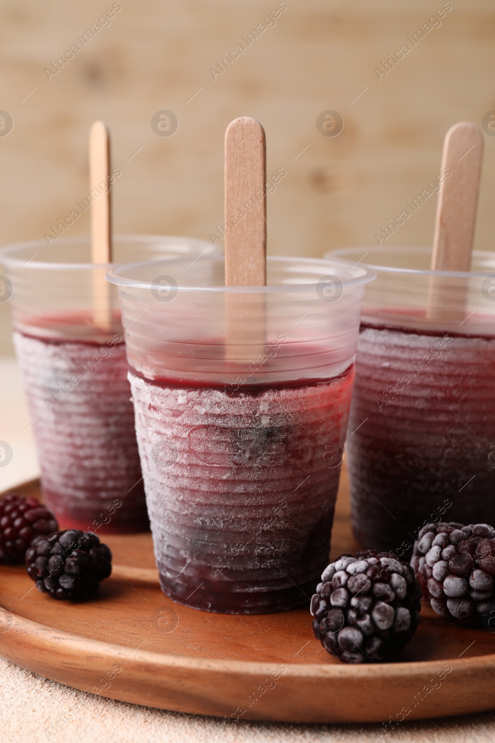 Photo of Tasty blackberry ice pops in plastic cups on white table, closeup. Fruit popsicle