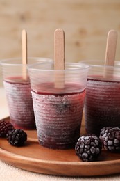 Photo of Tasty blackberry ice pops in plastic cups on white table, closeup. Fruit popsicle