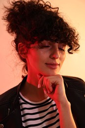 Photo of Beautiful young woman in black leather jacket posing on color background in neon lights