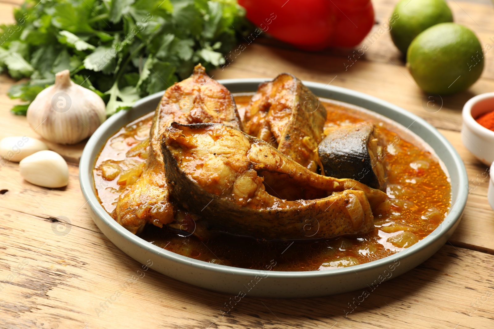 Photo of Tasty fish curry and ingredients on wooden table, closeup. Indian cuisine