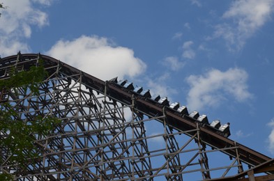 Photo of Amusement park. Beautiful large rollercoaster against blue sky, low angle view