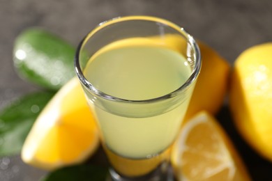 Photo of Tasty limoncello liqueur, lemons and green leaves on table, closeup