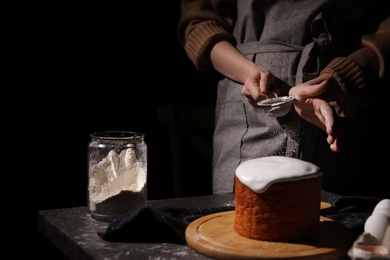 Photo of Young woman making traditional Easter cake at table against black background, closeup