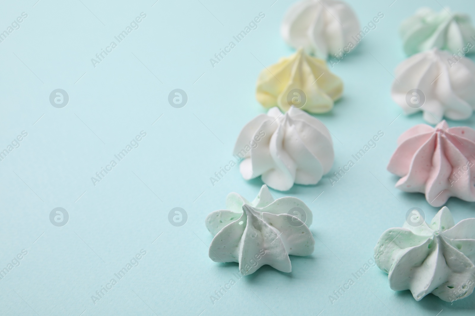 Photo of Delicious meringue cookies on light blue background, closeup. Space for text