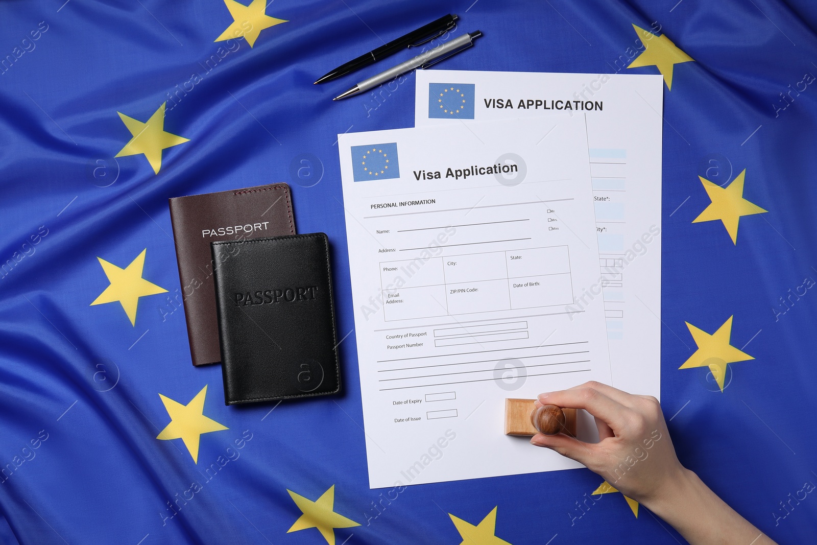 Photo of Immigration to European Union. Woman stamping visa application forms on flag, top view