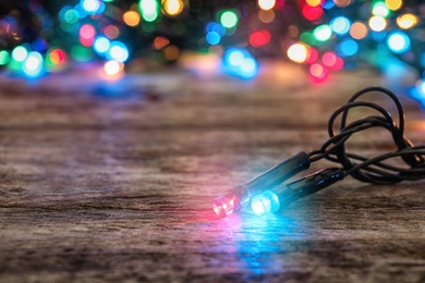 Glowing Christmas lights on wooden table, closeup