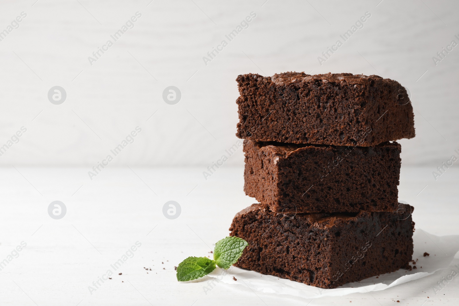 Photo of Parchment paper with fresh brownies on table against light background, space for text. Delicious chocolate pie