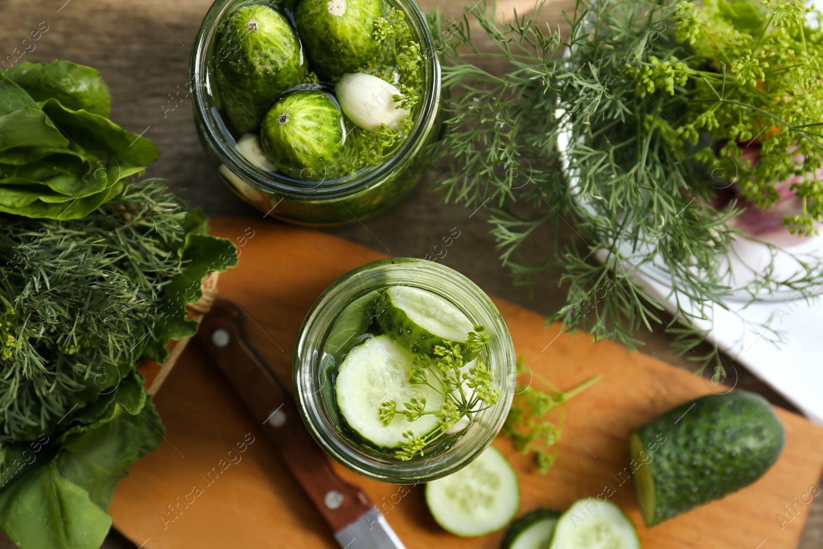 Photo of Glass jars, fresh cucumbers and herbs on wooden table, flat lay. Pickling recipe