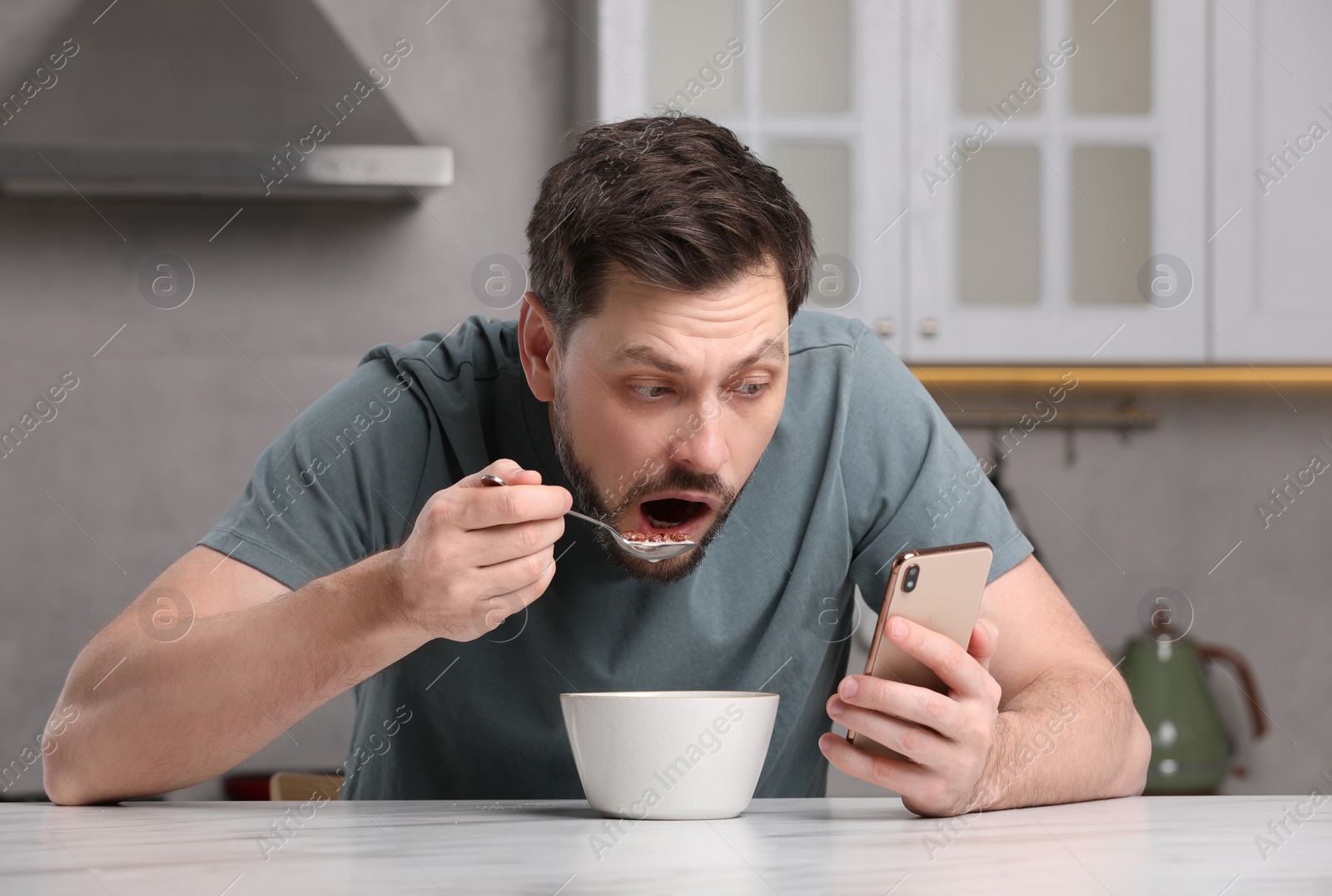 Photo of Man using smartphone while having breakfast at table in kitchen. Internet addiction