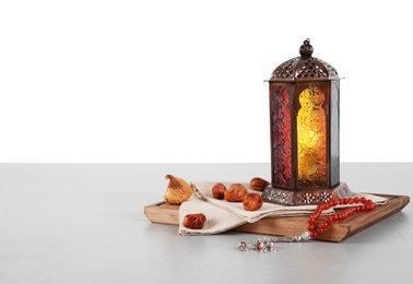 Photo of Muslim lamp, dates and prayer beads on table against white background. Space for text