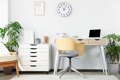 Photo of Beautiful workplace with laptop on white wooden table, chair and houseplants in room