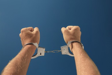 Photo of Man in handcuffs against blue sky outdoors, closeup