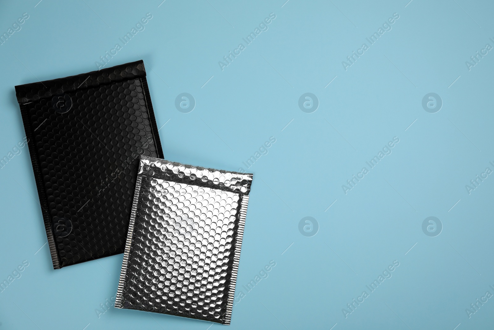 Photo of Two padded envelopes with bubble wrap on turquoise background, flat lay. Space for text