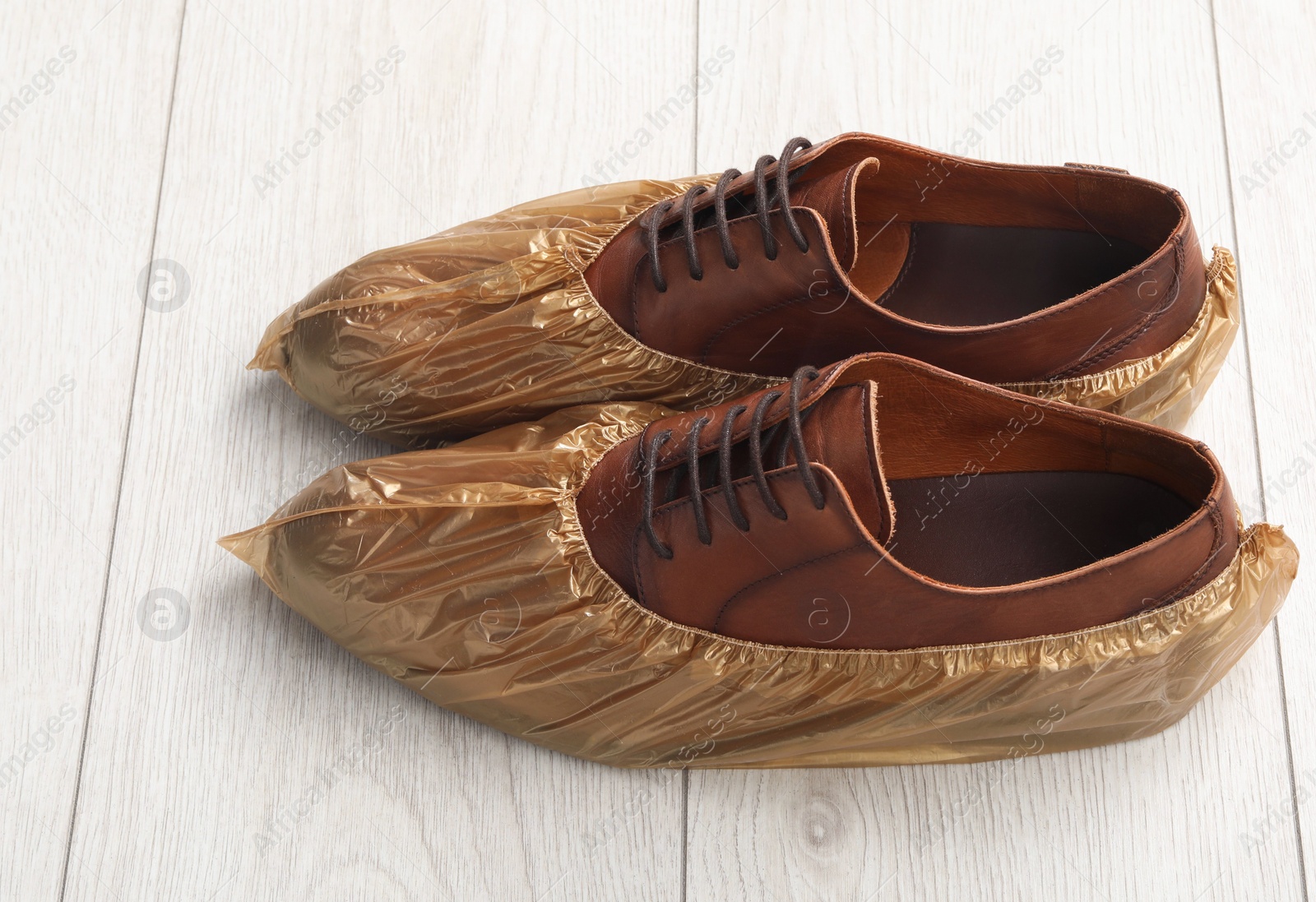 Photo of Men`s shoes in shoe covers on light wooden floor