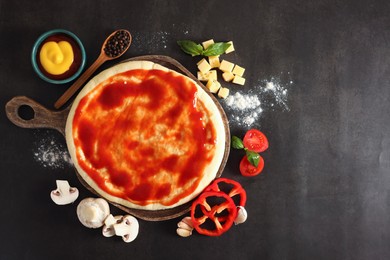 Photo of Pizza dough smeared with tomato sauce and products on dark table, flat lay. Space for text