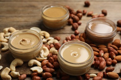Photo of Jars with butters made of different nuts and ingredients on wooden table, closeup