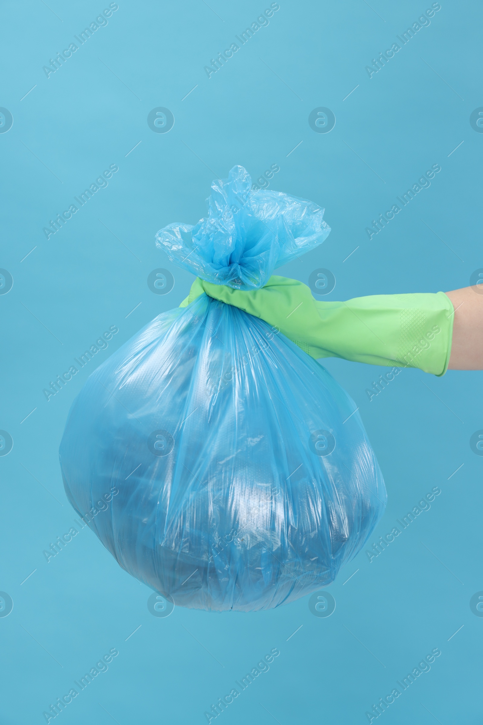 Photo of Woman holding plastic bag full of garbage on light blue background, closeup