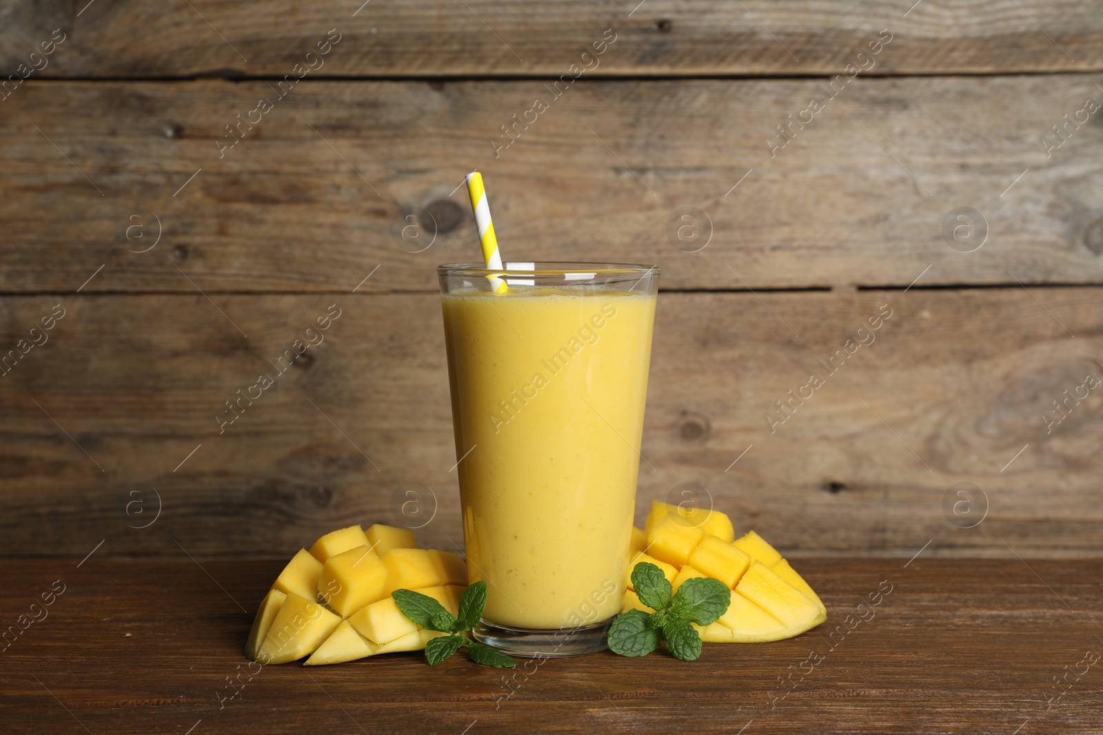 Photo of Glass of tasty smoothie with straw, mint leaves and mango on wooden table