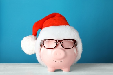 Photo of Cute piggy bank with Santa hat and glasses on table