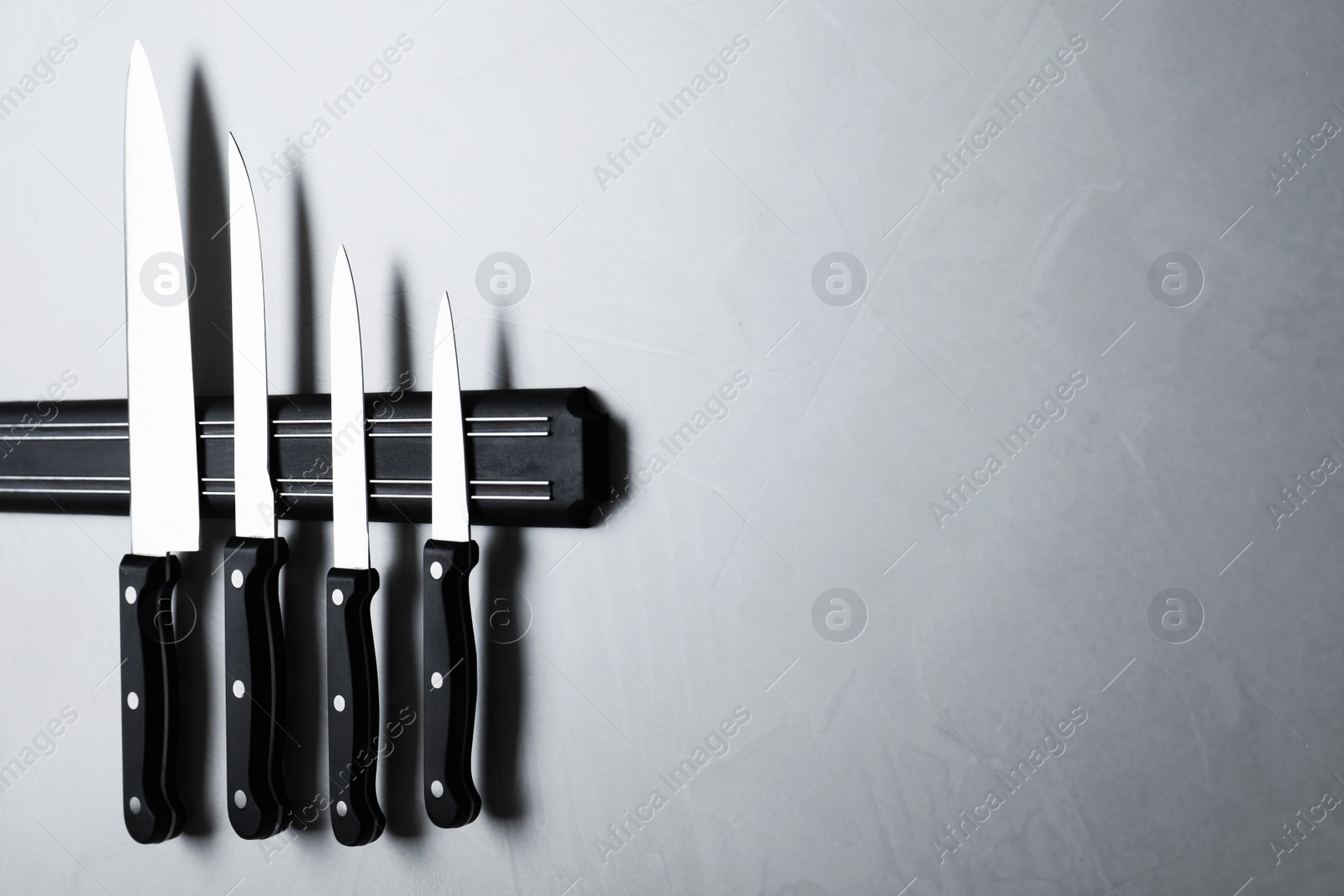 Photo of Magnetic holder with set of knives on grey stone background. Space for text