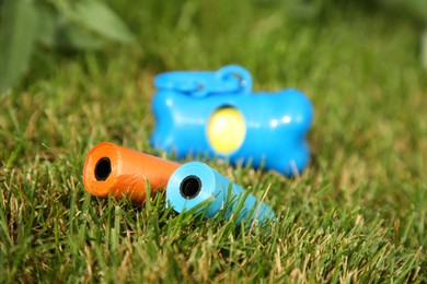 Rolls of colorful dog waste bags on green grass outdoors, selective focus