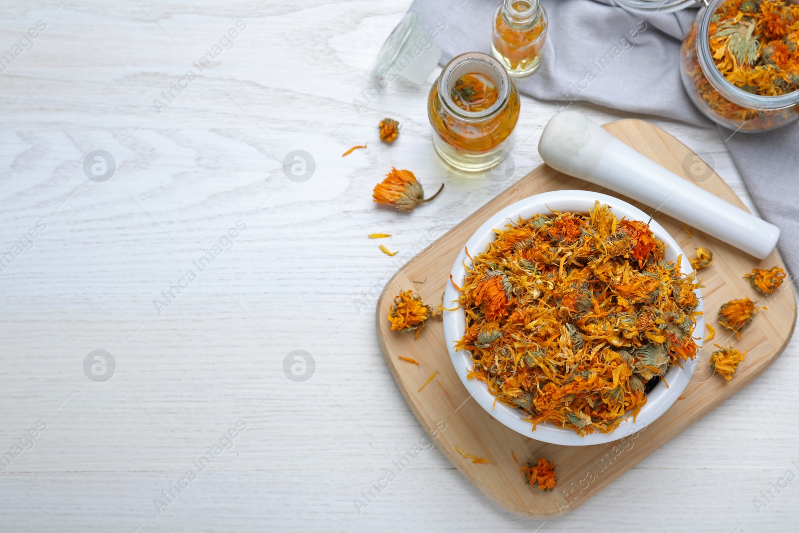 Photo of Dry calendula flowers and bottles with tincture on white wooden table, flat lay. Space for text