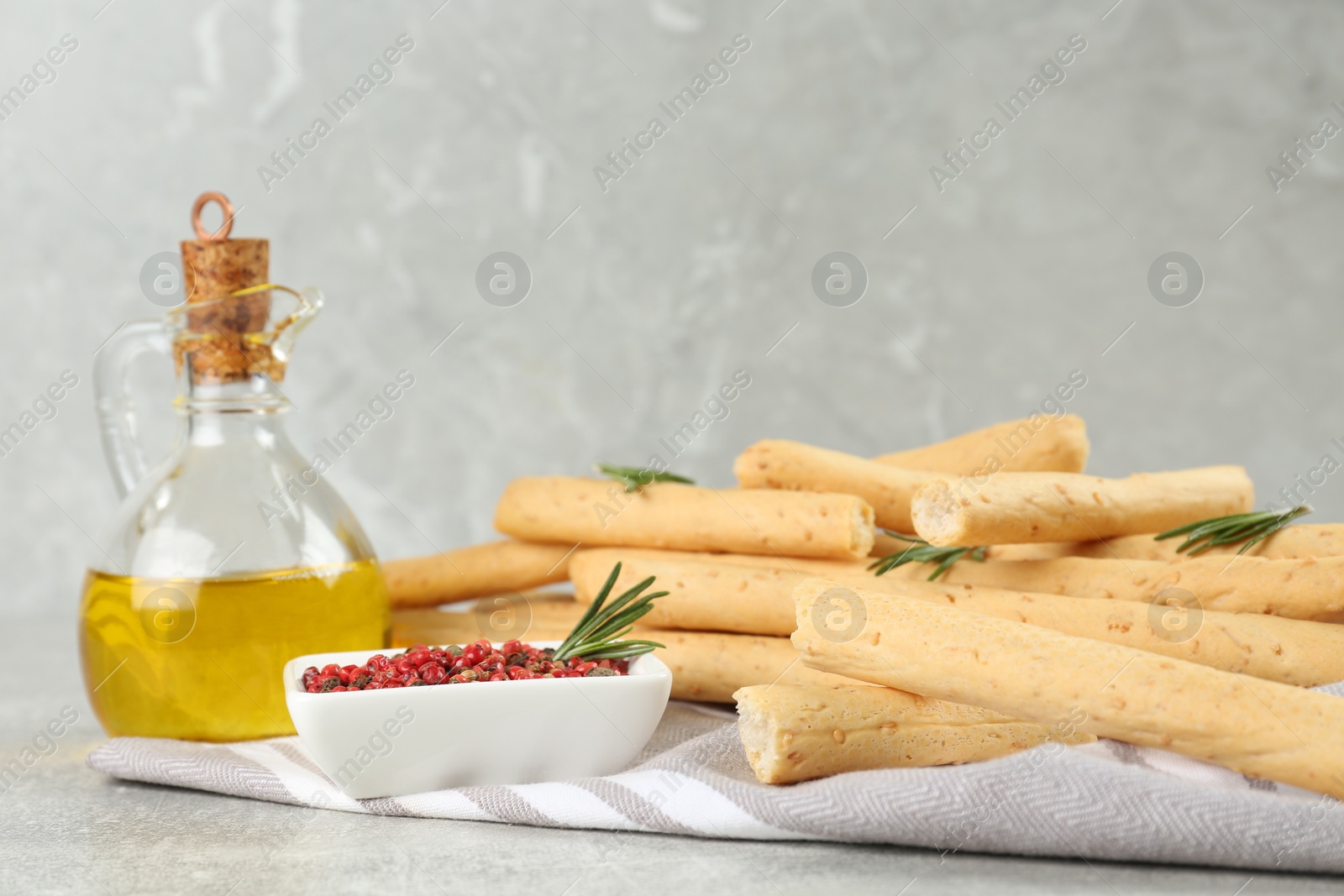 Photo of Tasty grissini with rosemary, pepper and oil on light grey table