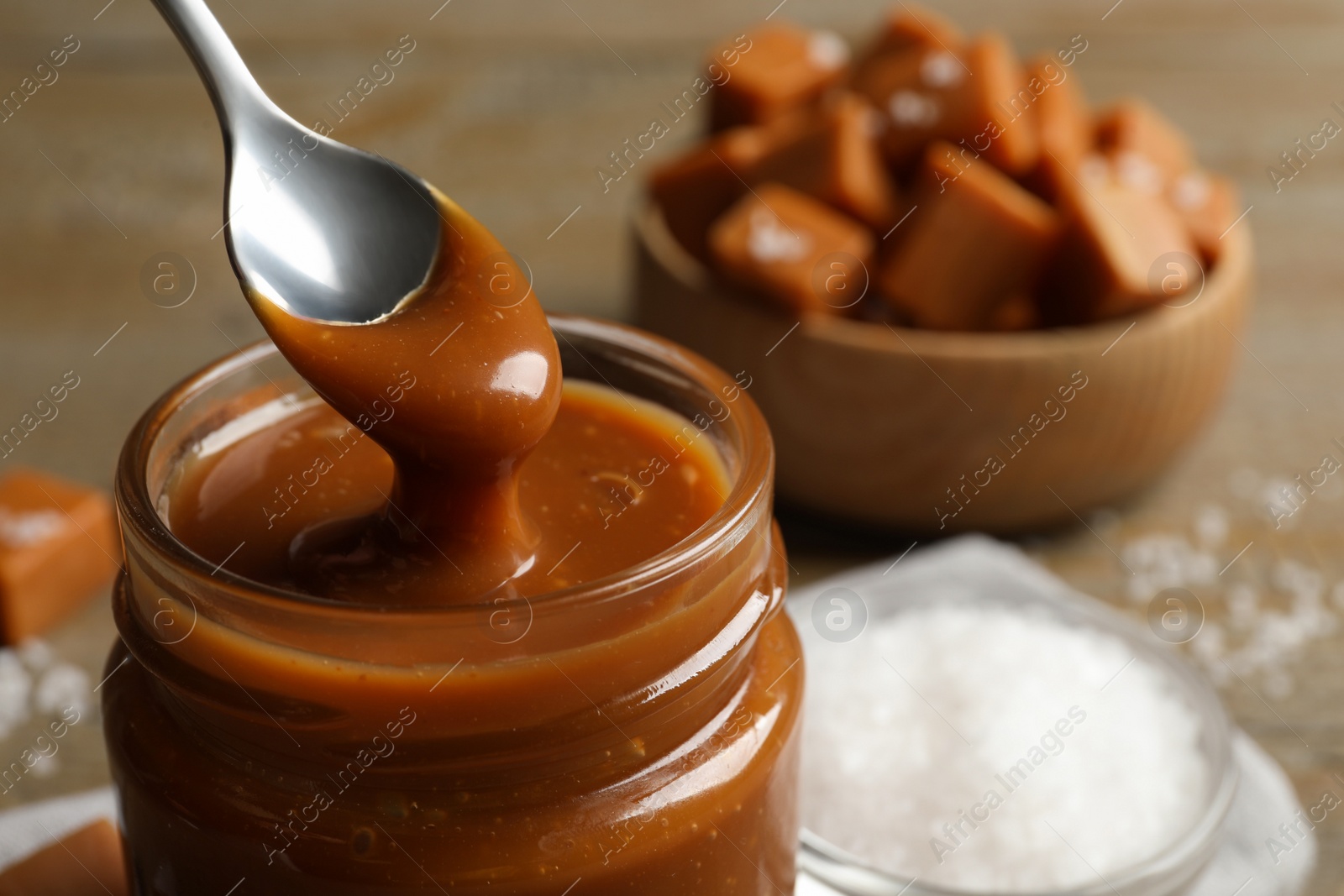 Photo of Taking yummy salted caramel with spoon from glass jar at table, closeup. Space for text